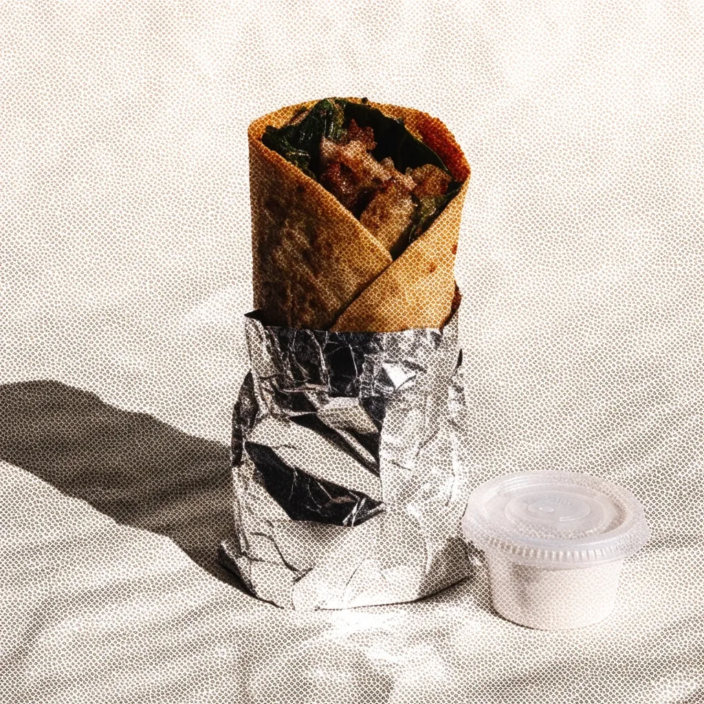 A foil-wrapped burrito on a plain paper liner, filling visible where the foil is folded back