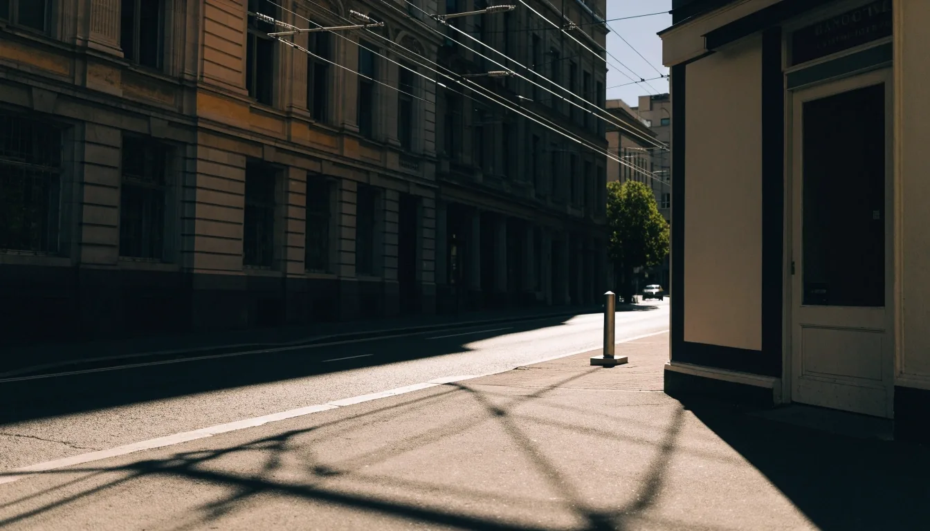 A quiet Melbourne street at noon with tram wires and hard shadows on the pavement